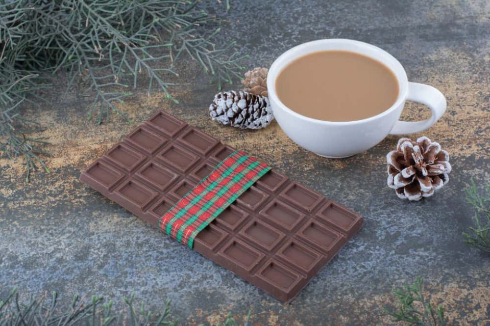 Barre de chocolat suisse au lait décorée pour Noël avec une tasse de café chaud et des pommes de pin sur une surface rustique.