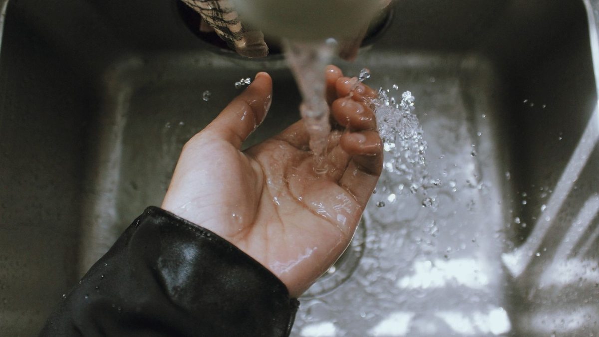Eau coulant sur une main ouverte au-dessus d'un évier en acier inoxydable