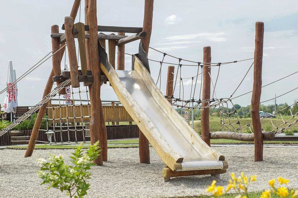 Structure de jeu en bois avec toboggan, filets et cordes, dans un parc Structure de jeu en bois avec toboggan, filets et cordes, dans un parc
